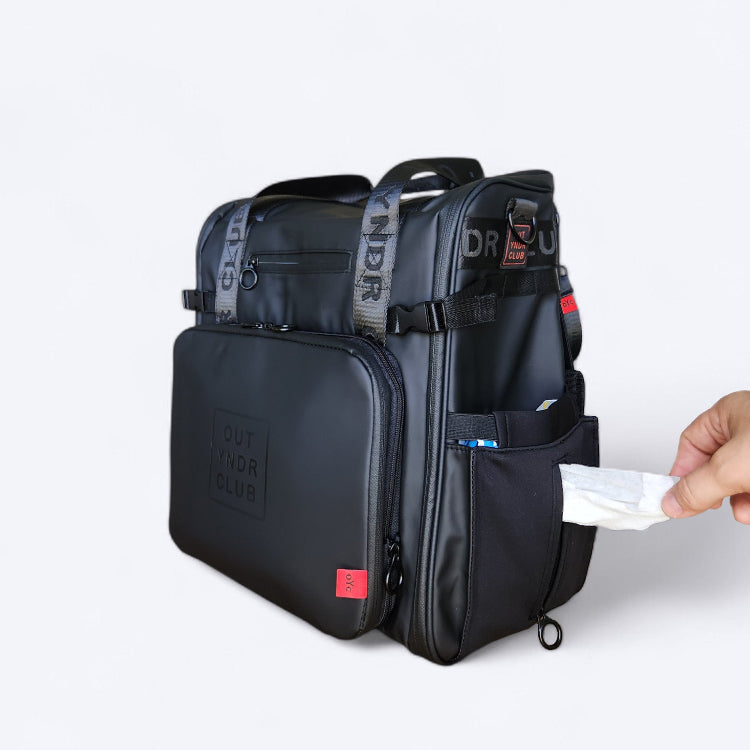 OUT YNDR CLUB Medley nappy backpack for Mum's with newborn baby, black side view removing wipes from zip pocket